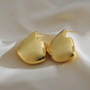 Macro shot of minimalist gold geometric teardrop earrings on elegant white satin fabric