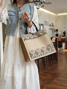 Detailed close-up of tribal geometric patterns on a natural jute tote bag with black handles