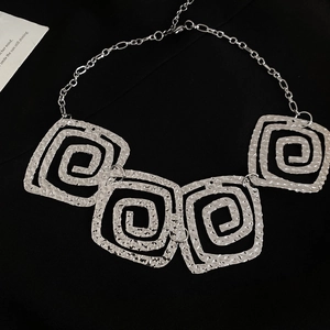 Detailed macro view of silver chain necklace with square textured spiral pendants
