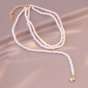 Detail of multi-layer white pearl necklace with gold heart pendant on silk background