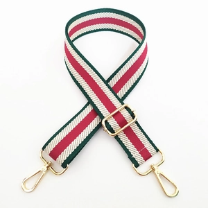 Detail of adjustable green, white, and red striped fabric bag strap with gold metal hardware