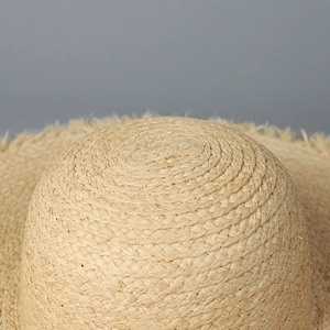 Gros plan du chapeau en raphia montrant le tissage détaillé et les bords effilochés