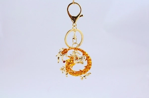 Detail of golden dragon keychain with orange gemstones and white pearl on white background