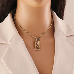 Golden rectangle pendant necklace with Greek key pattern and blue evil eye charm on model