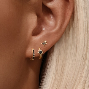 Close-up of gold ear set with black zircon hoop and star studs on a female ear