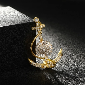 Elegant gold anchor brooch with sparkling zircon crystals on a black textured surface
