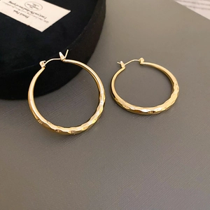 Detailed view of golden hoop earrings featuring textured faceted metal and a shiny finish