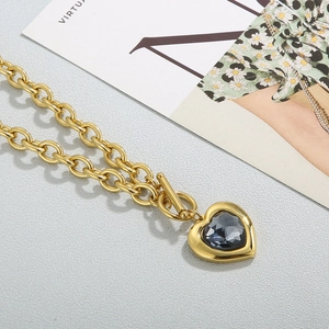 Detail of gold chunky chain necklace with a heart pendant and faceted grey crystal