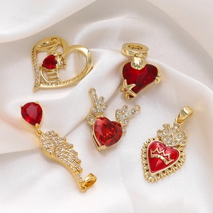 Detail of 18K gold plated wing and heart pendants with red zircon inlay on silk background