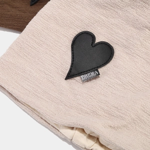 Detailed close-up of the beige knitted texture and heart leather patch with logo label