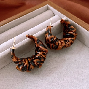 Macro detail of leopard print C-shape earrings with pleated texture in a jewelry box