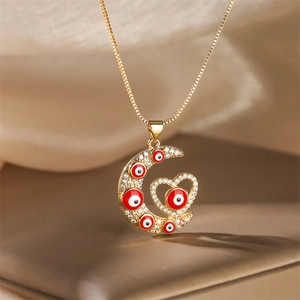 Détail du pendentif lune et cœur doré orné de pierres et d'un œil porte-bonheur