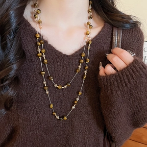 Detail of layered tiger eye stone beads and crystal pendants on a gold chain necklace