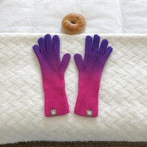 Close-up of gradient purple knit touch screen gloves with circular logo tag on white fabric