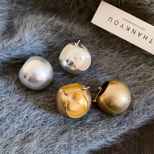 Close-up of gold and silver U-shaped basket earrings on a plush gray texture background