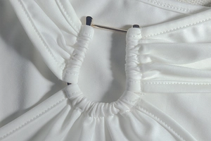 Detailed view of white ruched fabric with light gold U-shaped metal buckle detail