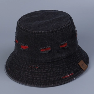 Detail of black denim bucket hat with distressed red torn effects and brown leather logo tag