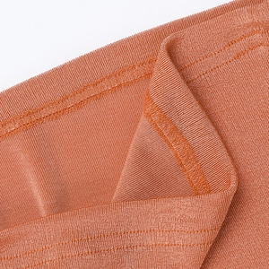 Close-up of rust orange knitted fabric showing detailed ruffle edges and fine stitching