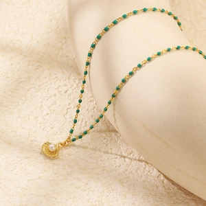 Detail view of a gold shell necklace with a white pearl inlay and green enamel beads