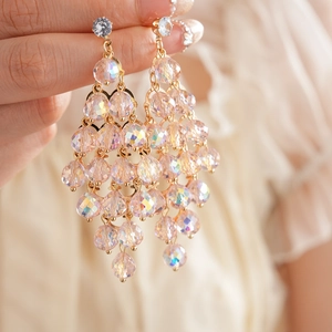 Makroaufnahme goldener Quastenohrringe mit rosa Kristallperlen in der Hand