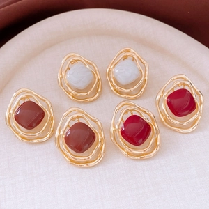 Detailed macro view of three pairs of geometric gold-plated resin stud earrings on a tray