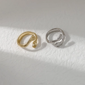 Minimalist hand hug open rings in gold and silver finish on white textured background