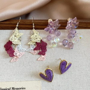 Detail view of purple resin flower studs and marble heart earrings on fabric