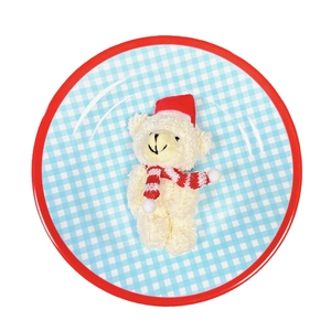 Christmas teddy bear plush on a red rimmed blue plaid plate with a festive hat and scarf