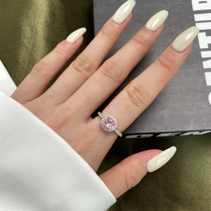 Macro view of a pink gemstone ring with white zircon halo on hand with velvet box