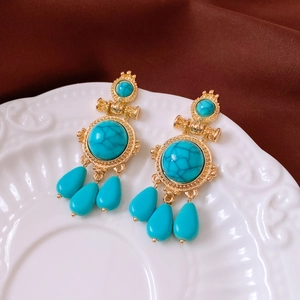 Detail of vintage gold earrings with turquoise stones and droplet charms on white ceramic