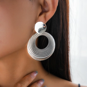Detailed close-up of large silver hollow round earrings featuring mesh texture and metal studs
