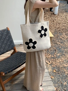 Close-up of beige knitted tote bag featuring black floral appliques and large capacity