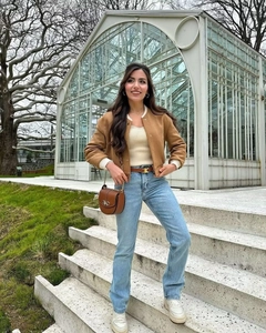 Outdoor street style view of a brown biker jacket paired with light blue denim pants