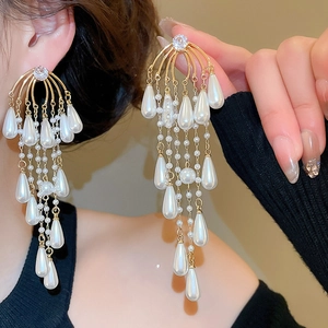 Close-up of elegant gold tassel earrings with drop pearls and zircon accents on model