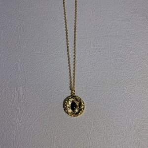 Detailed close-up of a vintage gold pendant necklace with black stone and texture