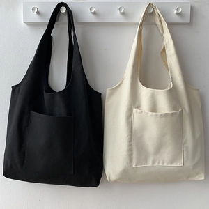 Detailed view of black and beige canvas tote bags with front pockets hanging on a wall