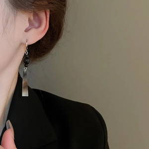 Detail of silver geometric rectangular earrings with black bead on a female model