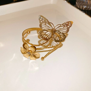 Detail of a gold metallic arm cuff featuring hollow butterfly and flower with a small crystal
