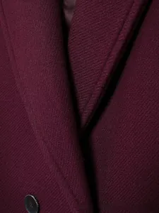 Détail du revers d'un manteau en laine bordeaux avec couture fine et bouton en résine
