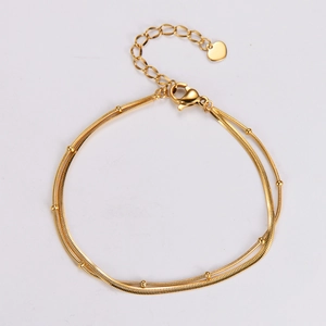 Detail of a double-layer gold snake chain bracelet with heart pendant and small round beads