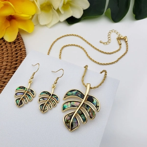 Golden monstera leaf jewelry set with colorful abalone shell inlay on white tropical background