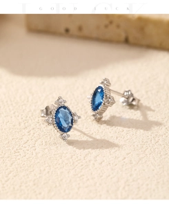 Close-up of vintage s925 silver stud earrings with oval blue gemstone on sandy texture