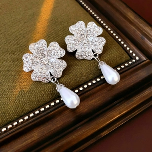 Detailed close-up of clover earrings with rhinestones and pearl drops on green velvet