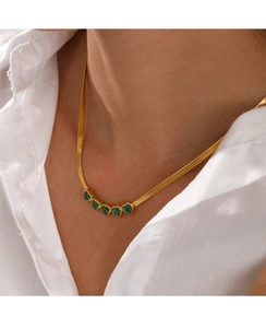 Close-up of gold snake chain necklace featuring five green heart-shaped gemstones