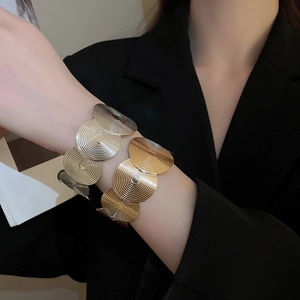 Close-up of gold and silver open bracelets with concentric spiral texture on black suit