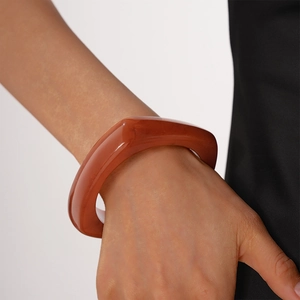 Detail of reddish-brown thick resin bangle showing translucent amber-like texture on wrist
