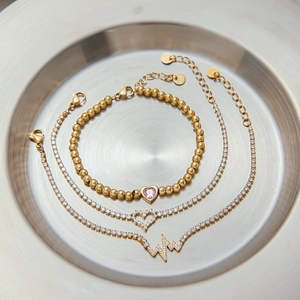 Close-up of gold heart and heartbeat pendants on zircon tennis chains in a metal tray