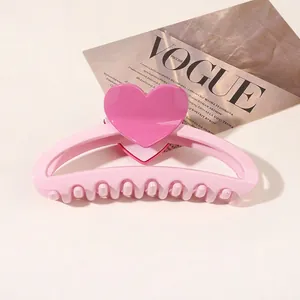 Detail of pink heart hair claw clip with glossy finish resting on a beige background