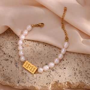 Macro shot of freshwater pearl bracelet with gold 11:11 plaque on silk and stone
