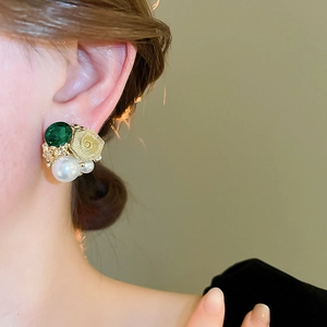 Gros plan de boucles d'oreilles rose dorée avec pierres vertes et perles